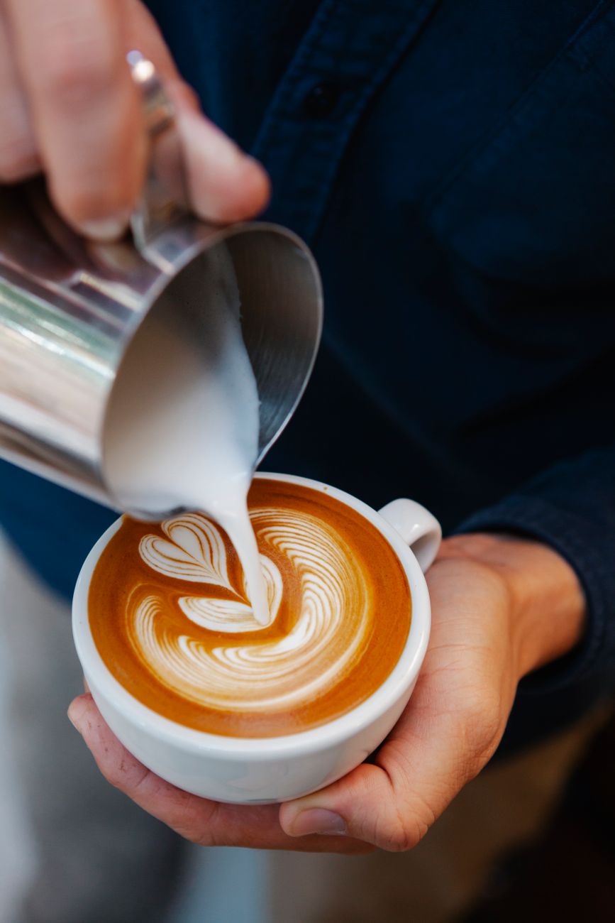 Barista experiente derramando leite fresco com leite arte em copo